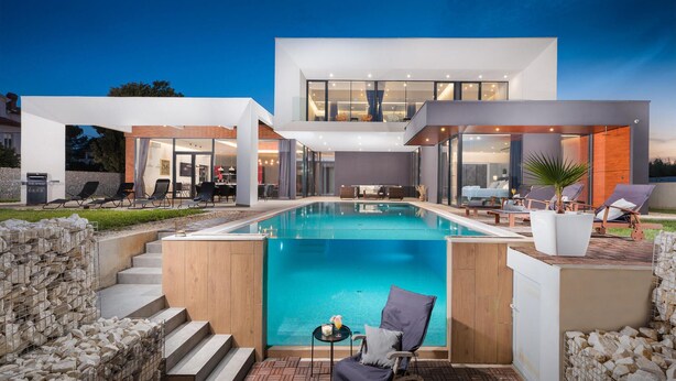Una casa moderna con piscina, mobiliario exterior y una escalera que lleva a la planta superior.