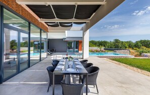 Un espace extérieur aménagé pour les repas, avec une table dressée pour six personnes, donnant sur une piscine et offrant une vue panoramique.