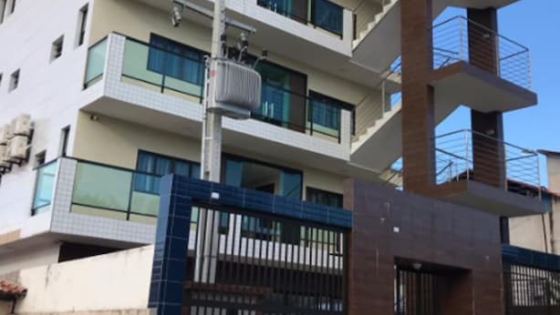 Un immeuble résidentiel à plusieurs étages, doté de balcons, d’une entrée sécurisée et d’un poteau électrique auquel sont fixés divers équipements.
