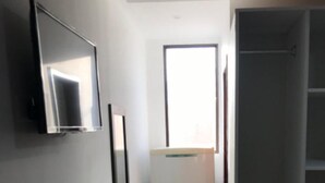 Un couloir étroit avec un réfrigérateur blanc, un miroir et une porte donnant sur une pièce avec une fenêtre.