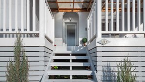 Un bâtiment blanc avec un escalier menant à une porte, le numéro 20 étant situé sur le côté droit, et une petite plante sur les marches.