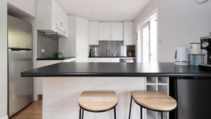 Une cuisine moderne avec des meubles blancs, un plan de travail noir, des appareils en acier inoxydable et deux tabourets en bois.