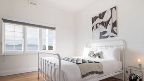 Une chambre avec un lit en métal blanc, une grande fenêtre donnant sur un beau paysage et un coussin à motifs zébrés.