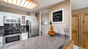 A modern kitchen with granite countertops, stainless steel appliances, and a chalkboard sign that reads "Welcome to Bee Camp."