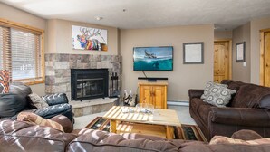 A living room with a stone fireplace, leather sofas, a wooden coffee table, and a television mounted on the wall.