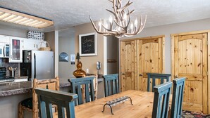 A dining area with a wooden table and chairs, a chandelier, and wooden doors.