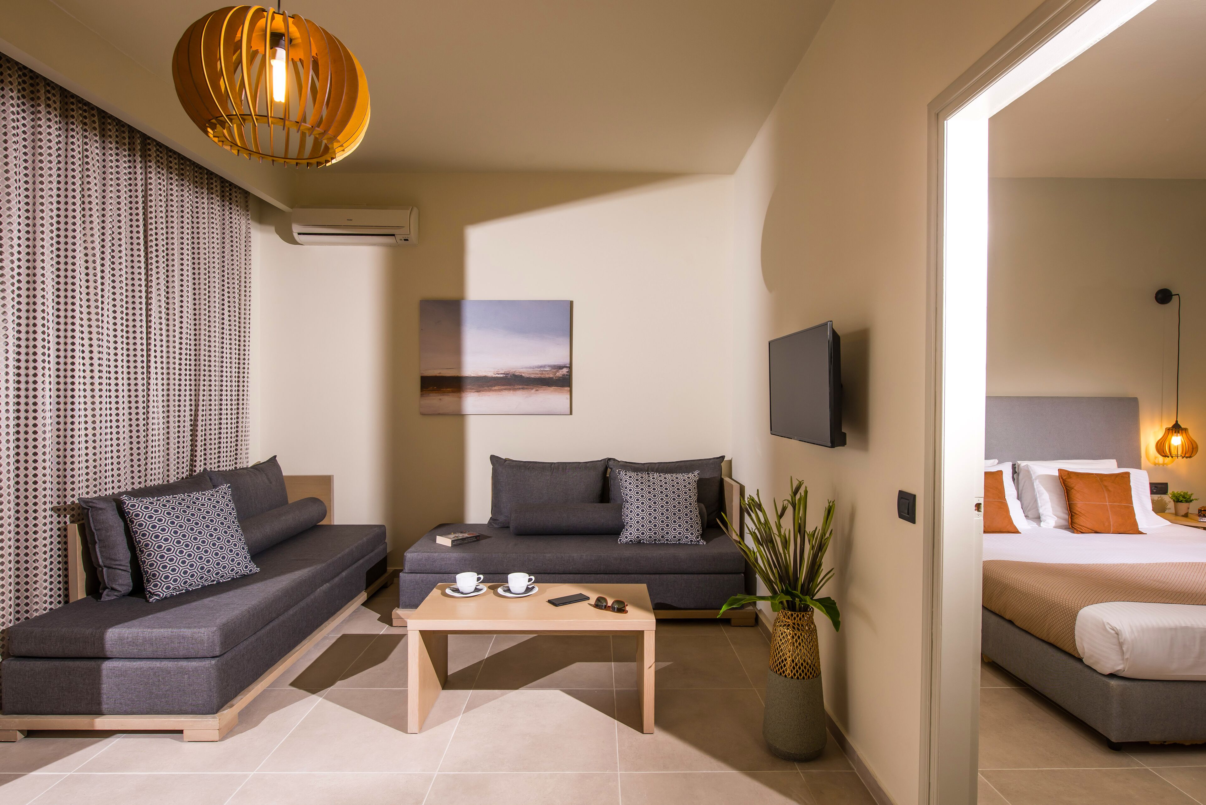 A modern hotel room with a sofa, a small table with cups, a TV, and a bed.