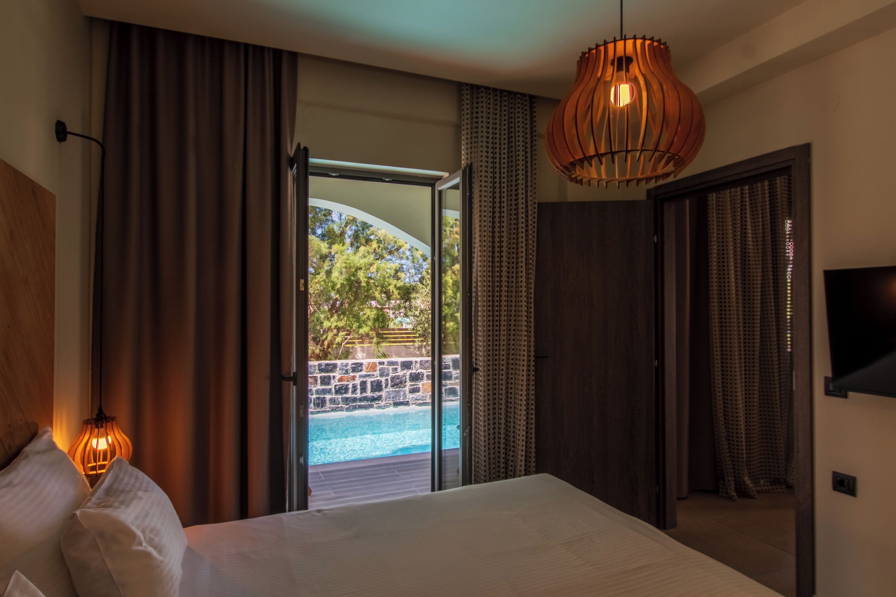 Un dormitorio con una cama grande, vista a una piscina exterior y una lámpara de techo de madera.