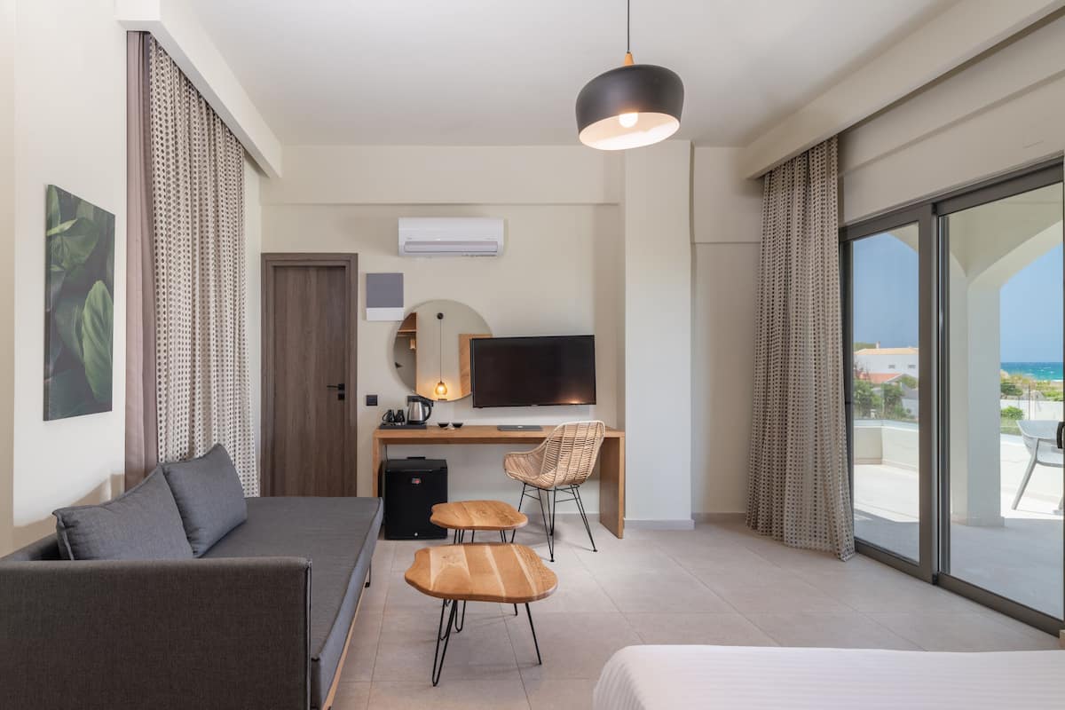 Une chambre d’hôtel moderne équipée d’un lit, d’un canapé, d’un bureau avec une chaise, d’une télévision et d’un balcon avec vue.
