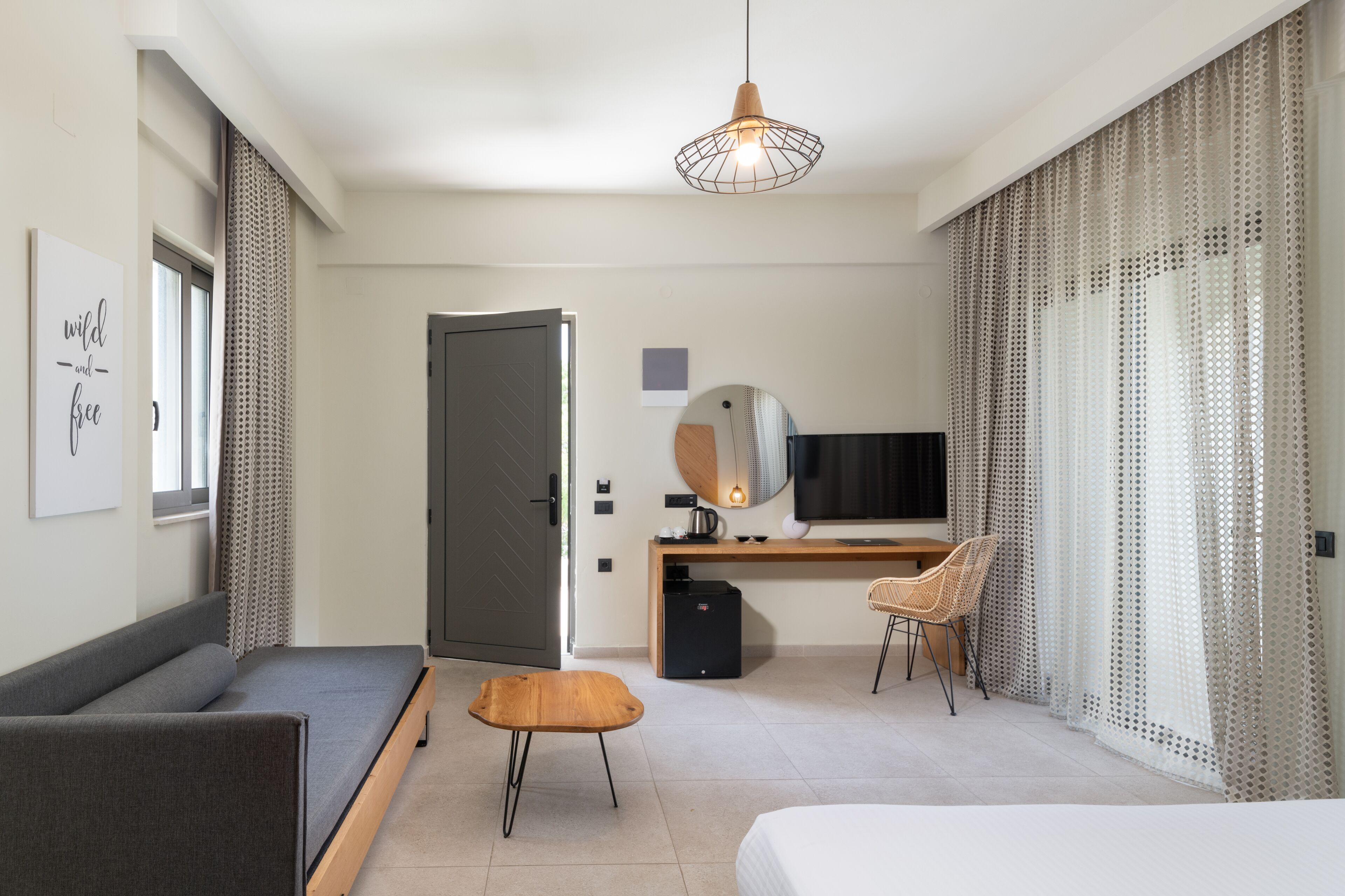 Ein modernes Hotelzimmer mit Bett, Schreibtisch, Stuhl, kleinem Tisch, Fernseher und einer Tür.