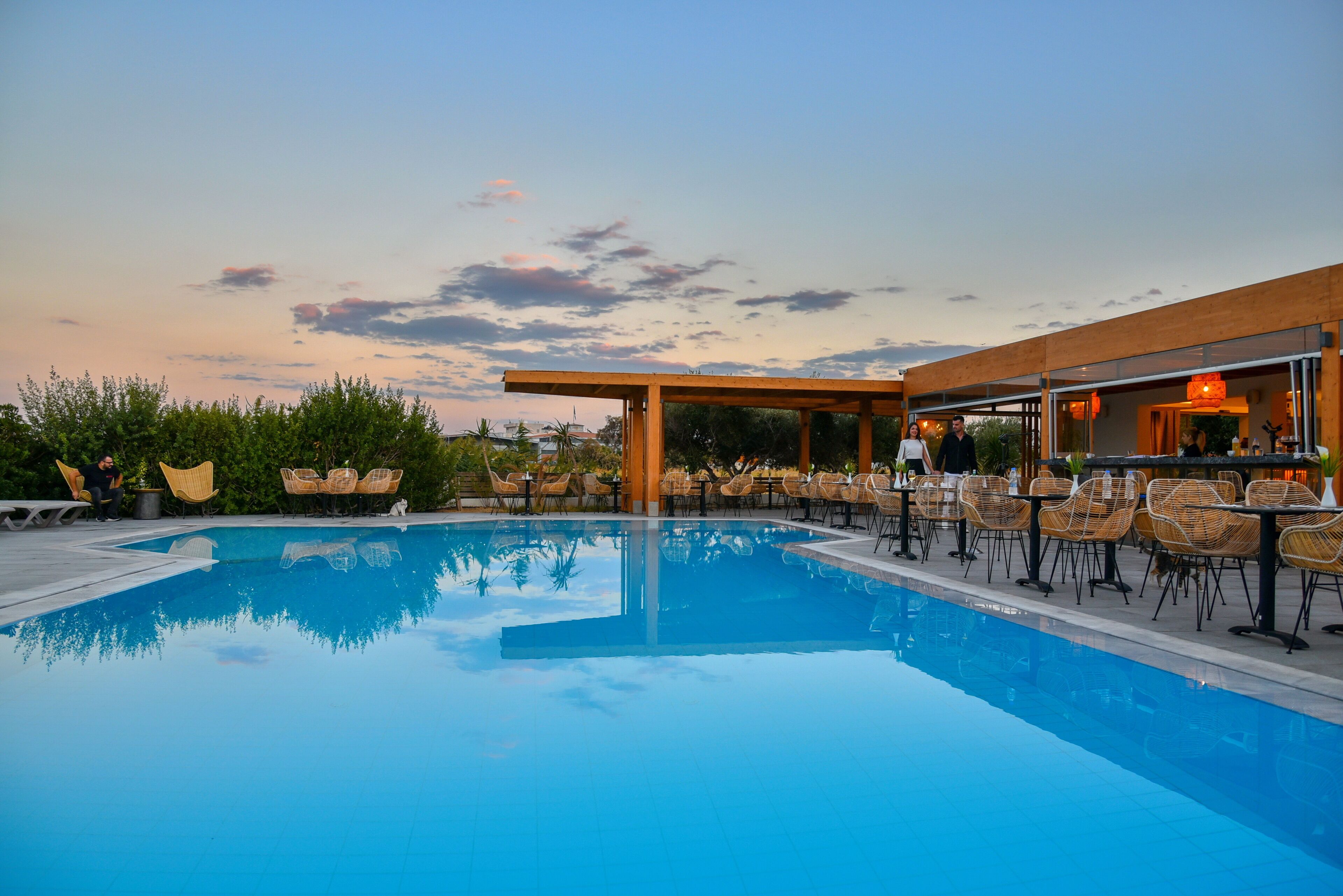 Une piscine entourée de verdure et agrémentée d’une pergola en bois, avec des chaises longues et des tables à proximité.