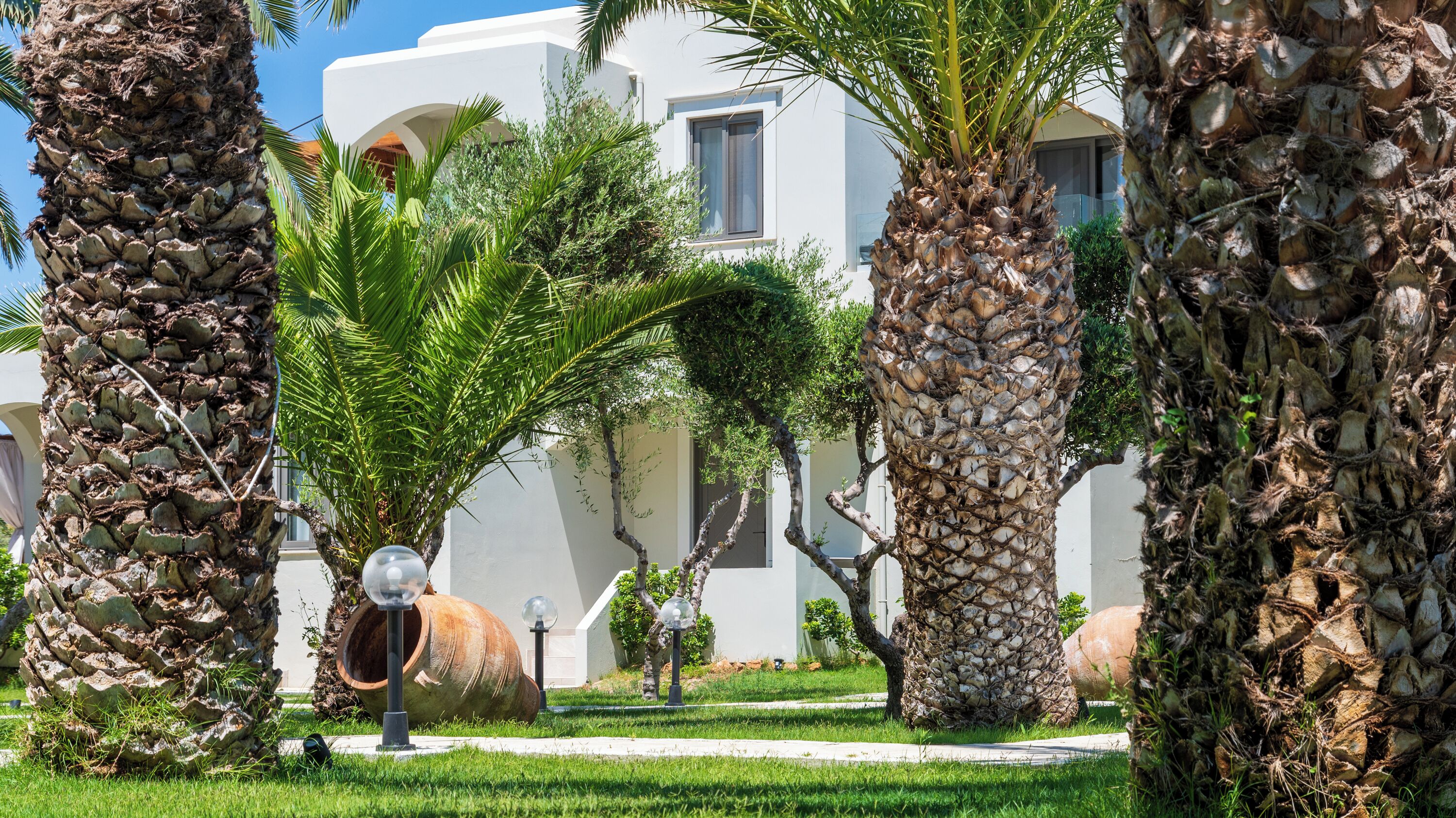 A well-maintained garden with palm trees and a pathway leading to a building with a modern architectural style.