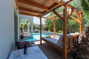 Una terraza de madera con piscina, una silla de descanso y una mesa con una botella y vasos.
