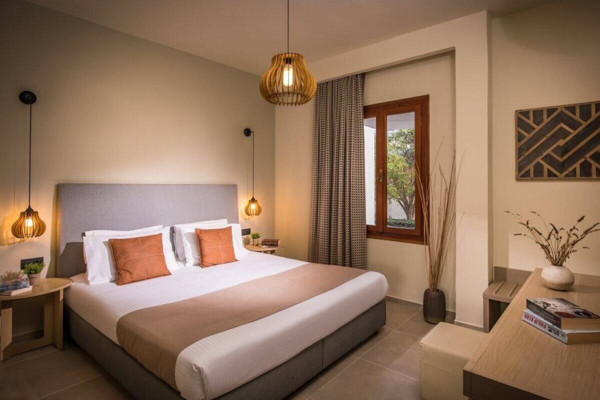 Une chambre d’hôtel moderne avec un grand lit, des tables de chevet, un bureau et une fenêtre avec des rideaux.