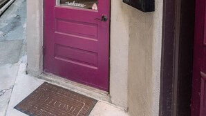 En rød dør med et 'Welcome'-skilt og en krans, en postkasse og en dørmåtte.