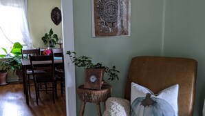 A cozy living room with a brown leather armchair, a wooden coffee table, and a dining area with a table and chairs. - Cozy cottage with backyard firepit (Asheville)