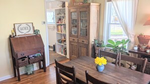 A dining area with a wooden table, chairs, and a vase of yellow flowers. There is a cabinet with glass doors and a bookshelf filled with books and decorative items. - Cozy cottage with backyard firepit (Asheville)