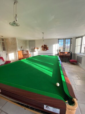 A pool table in a room with stone walls, a wooden bench, and a window with a view.