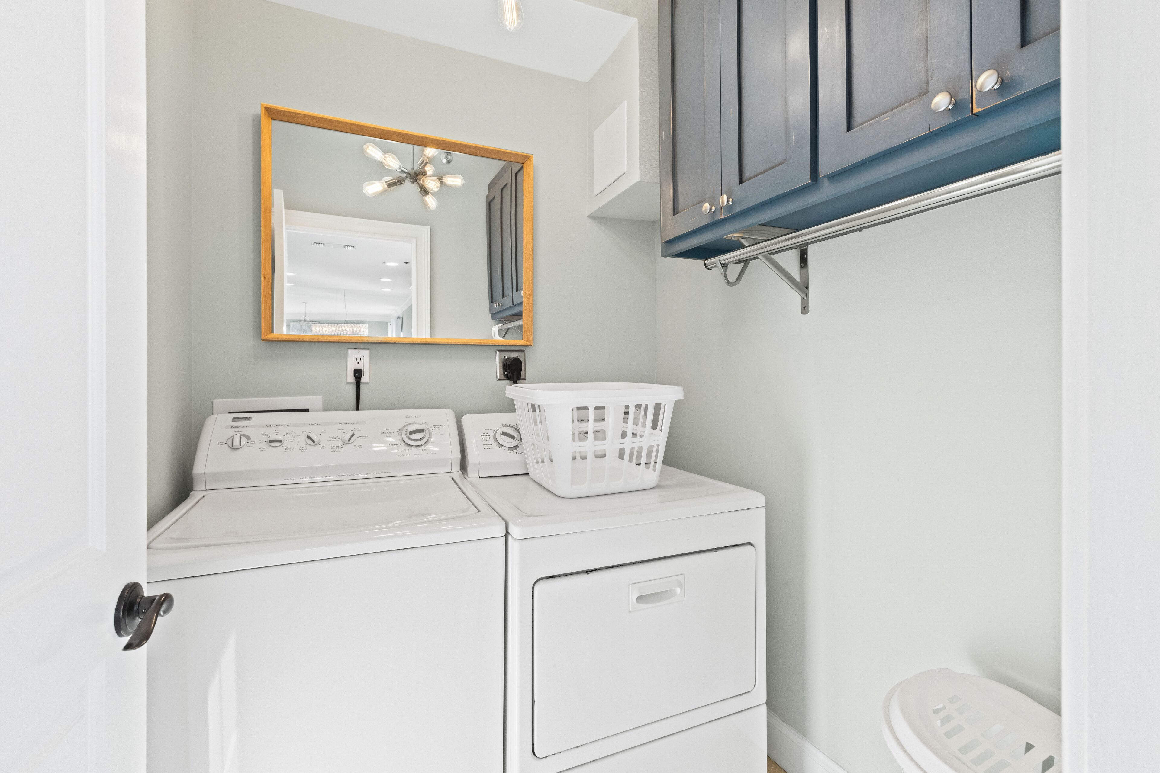 A laundry area with two stacked washers and dryers, a wooden-framed mirror, and a white laundry basket on the dryer.