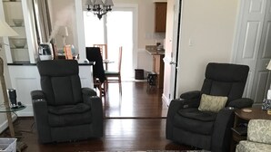 Een woonkamer met twee zwarte fauteuils, een kamerbreed tapijt en een witte hond met een rode bal.