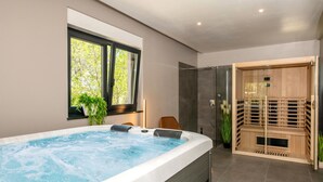 Ein modernes Badezimmer mit Whirlpool, Duschkabine aus Glas und einer Holzsauna.