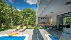Ein moderner Poolbereich im Freien mit Esstisch und Stühlen, umgeben von üppiger Bepflanzung.