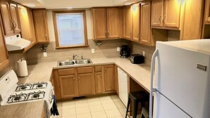 A kitchen with wooden cabinets, a sink, a stove, a dishwasher, a refrigerator, and a window with blinds. - South Wind, walk to the beach, zoo, & more! (Michigan City)