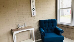 A room with a blue armchair, a white console table with a 'Beach' sign, and a 'WELCOME' sign on the wall. - South Wind, walk to the beach, zoo, & more! (Michigan City)