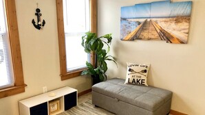 A cozy living room with a grey sofa, a plant, a bench, and a painting of a beach scene. - South Wind, walk to the beach, zoo, & more! (Michigan City)
