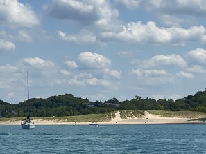 A sailboat on a calm sea with a beach and forested hills in the background. - South Wind, walk to the beach, zoo, & more! (Michigan City)