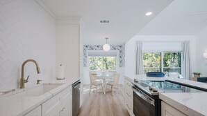 Een moderne keuken met witte kasten, een centraal eiland en een eetgedeelte met een ronde tafel en stoelen.