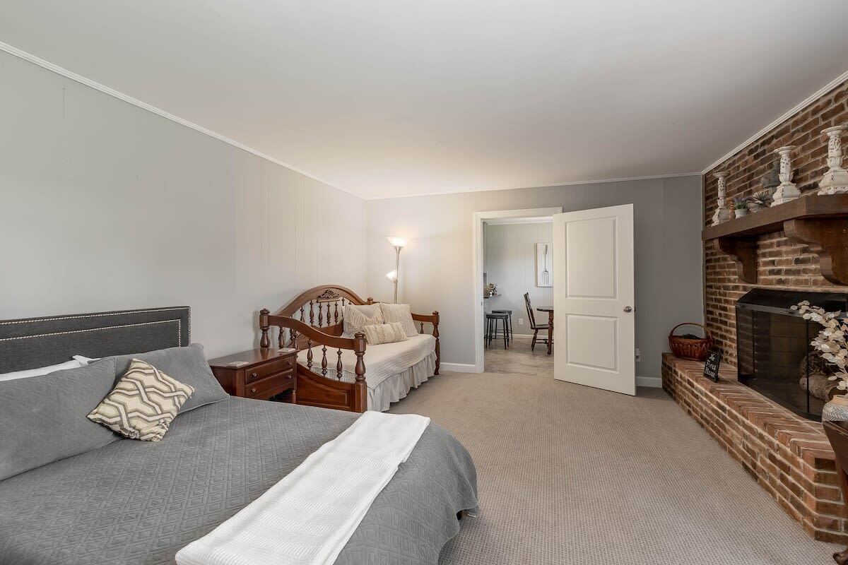 A bedroom with a bed, a dresser, a nightstand, a fireplace, and a door leading to another room.