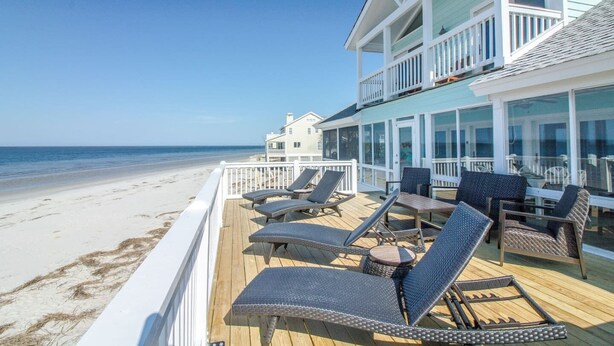A beachfront property with a deck featuring lounge chairs and tables, overlooking the ocean. - Harbor Point Ocean Front Beach Estate (Saint Helena Island)