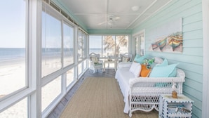 A coastal room with a white wicker sofa, a small table, and a view of the beach. - Harbor Point Ocean Front Beach Estate (Saint Helena Island)