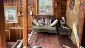Interior acolhedor de uma cabana com paredes de madeira, um banco estofado e uma janela com vista para o verde.