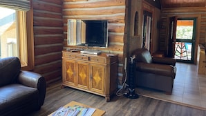 Interior de cabana de madeira com armário de madeira, sofá de couro e televisão em parede de madeira.