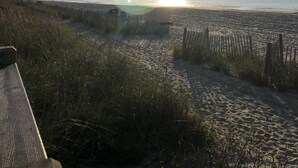 En strandscen med en klar himmel, en lågt hängande sol vid horisonten och ett trästaket i förgrunden.
