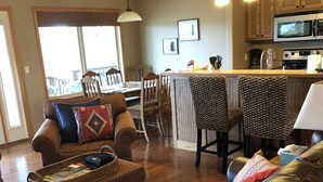 A cozy living room with a brown leather sofa, a wicker ottoman, and patterned chairs. A dining area with a wooden table and chairs is visible in the background. - Best view of the river! (Calico Rock)