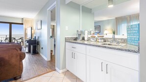 A modern kitchen with white cabinets, granite countertops, and a large window overlooking the ocean. - Ocean Front Condo in Ormond By The Sea ( Ormond Beach )  (Ormond Beach)
