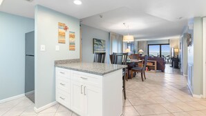 A modern kitchen with white cabinets and granite countertops, a dining area with a table and chairs, and a view of the ocean through large windows. - Ocean Front Condo in Ormond By The Sea ( Ormond Beach )  (Ormond Beach)