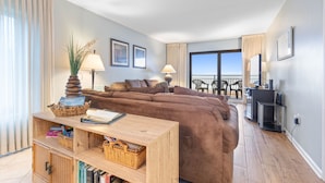 A modern living room with a brown sofa, a wooden coffee table, and a balcony with a view. - Ocean Front Condo in Ormond By The Sea ( Ormond Beach )  (Ormond Beach)