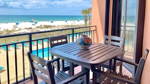 Un balcón con mesa y sillas, con vista a una piscina y una playa.