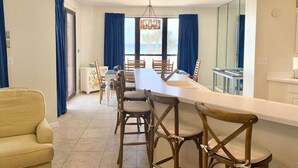Un comedor amplio con una mesa larga y sillas, un sofá y una zona de cocina con mostrador y armarios.