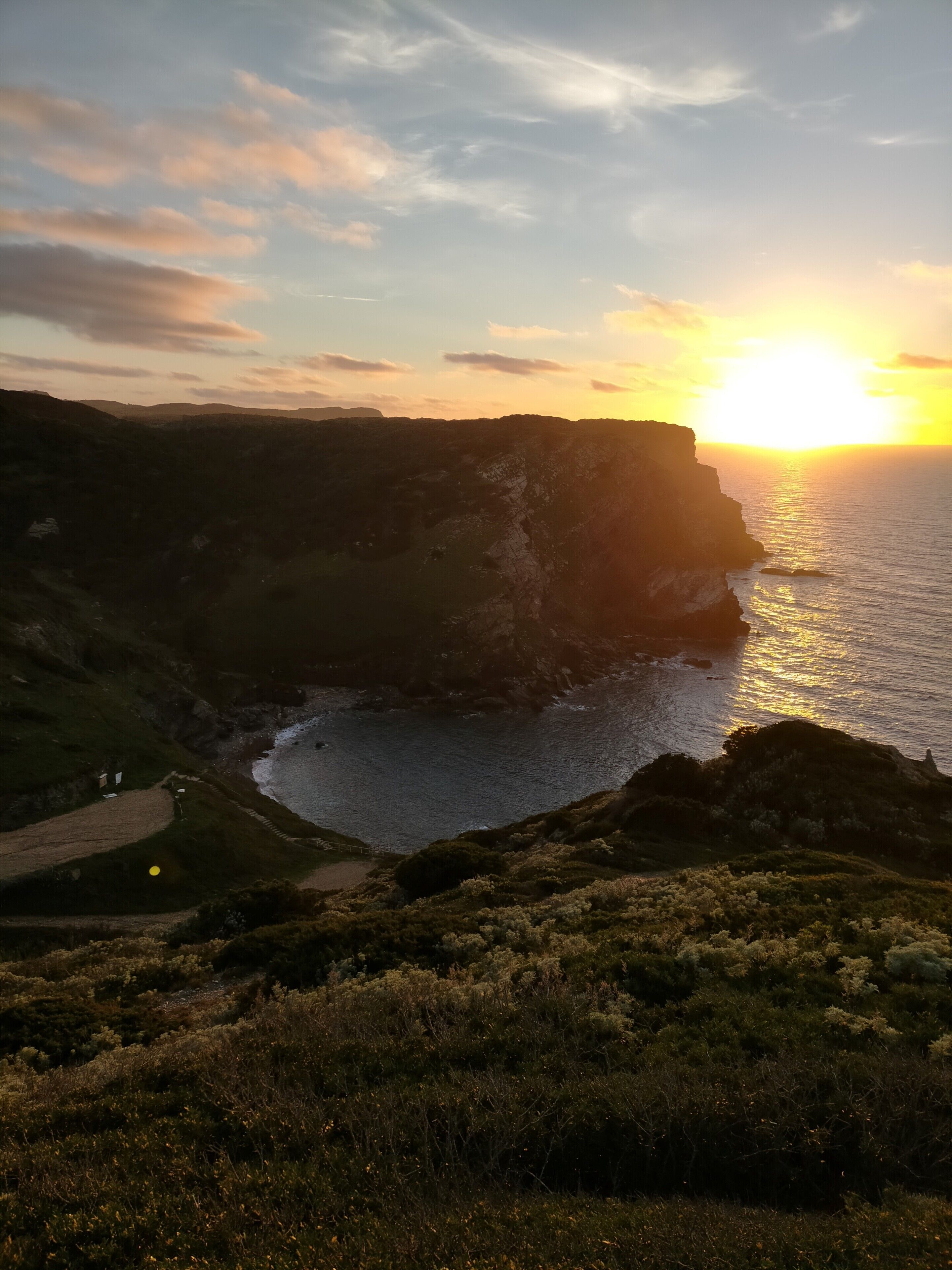 Un paysage côtier avec des falaises, un sentier et un coucher de soleil.