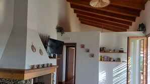 A living room with a stone fireplace, wooden beams, a television mounted on the wall, and a bookshelf with books and decorative items.