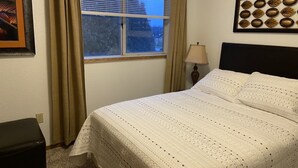 Una cama bien hecha con una colcha estampada, una lámpara de noche y una ventana con cortinas.