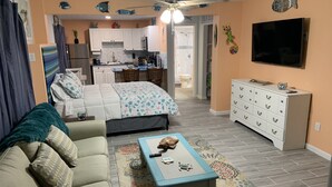 A compact living space with a sofa, a coffee table, a TV, a kitchen area, and a bathroom visible through an open door.