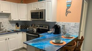 A kitchen with white cabinets, a stainless steel microwave, and a blue countertop island with chairs.