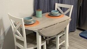 A dining table with two white chairs, a teal container, and a blue bowl on a plate.