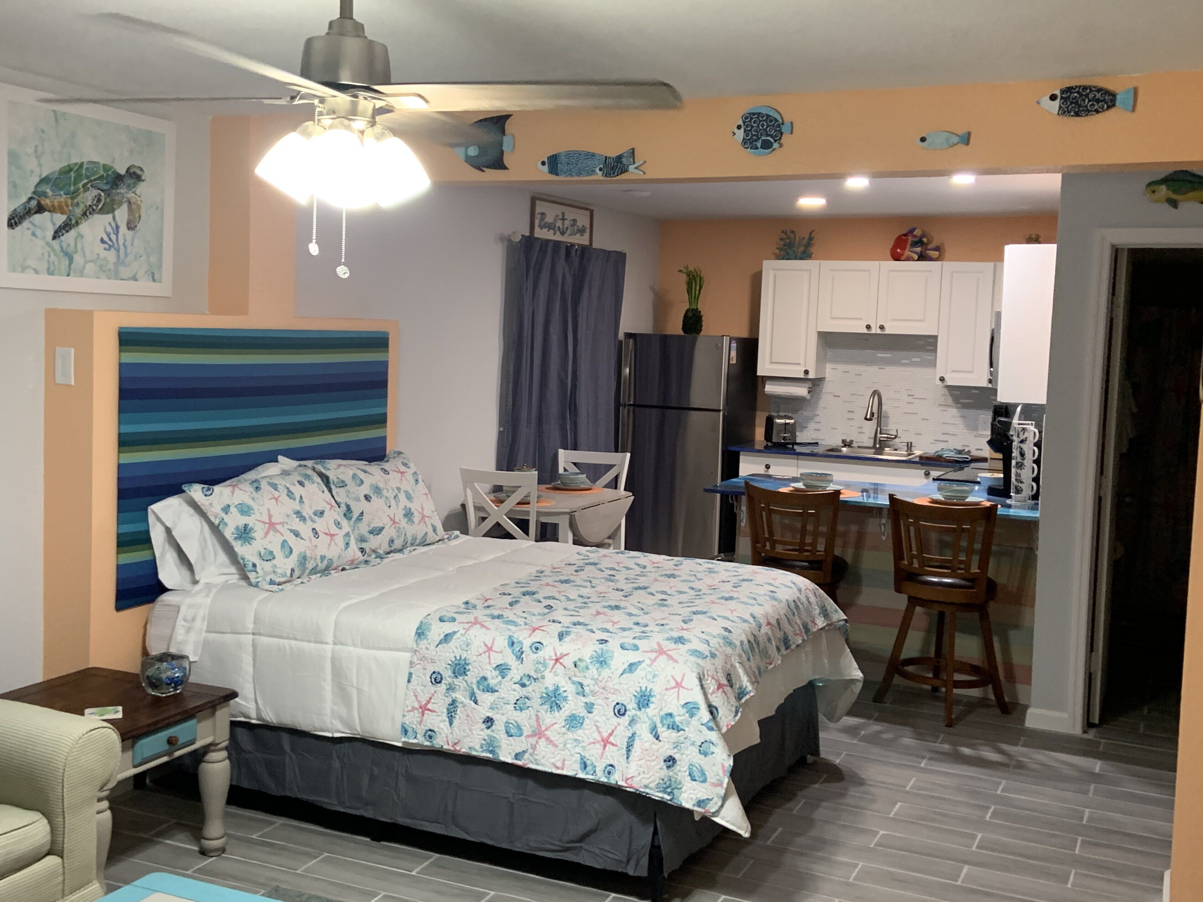 A bedroom with a bed, a desk, and a kitchenette.